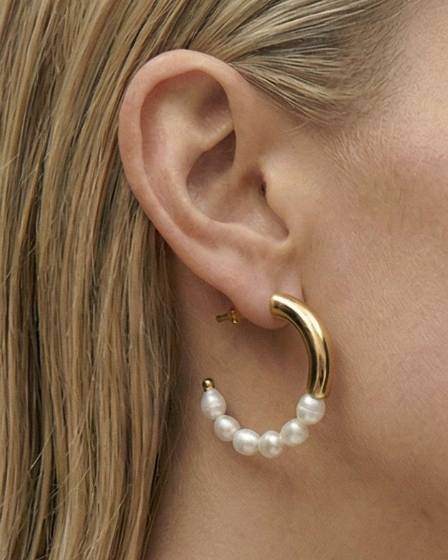 Side profile of a woman wearing a pearl earring against a plain background