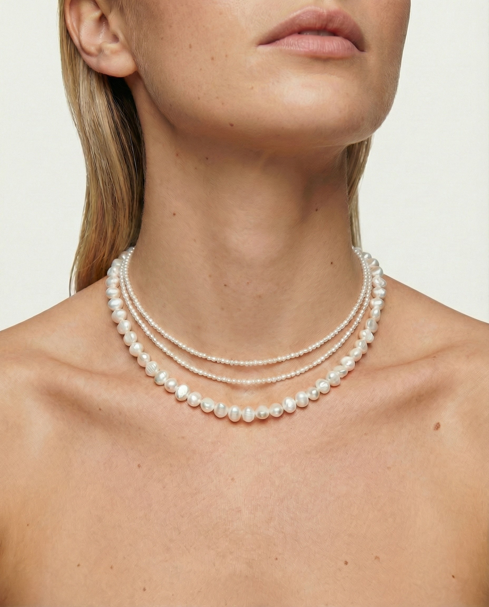 Woman wearing a pearl necklace against a neutral background
