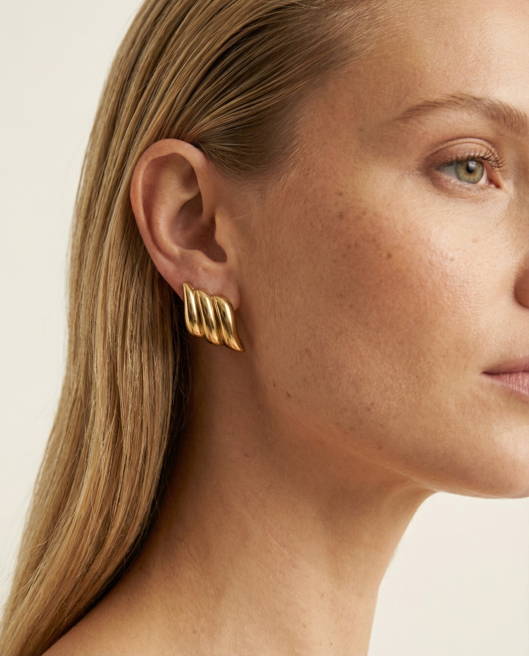 Close-up of a person wearing gold earrings with a neutral background