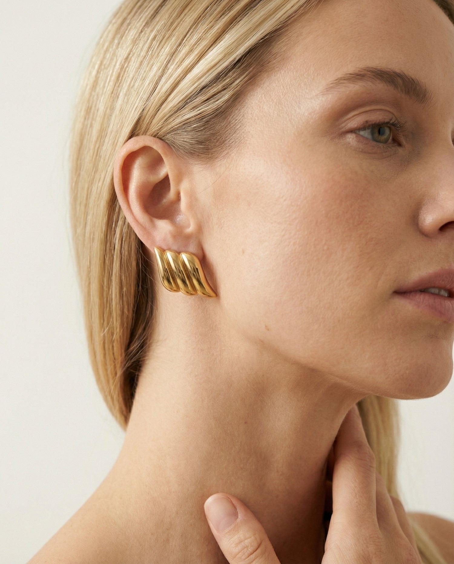 Close-up of a woman wearing gold hoop earrings with a neutral background