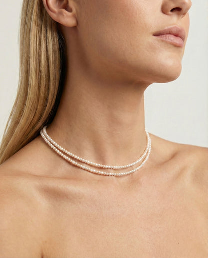 Close-up of a woman wearing a pearl necklace against a neutral background