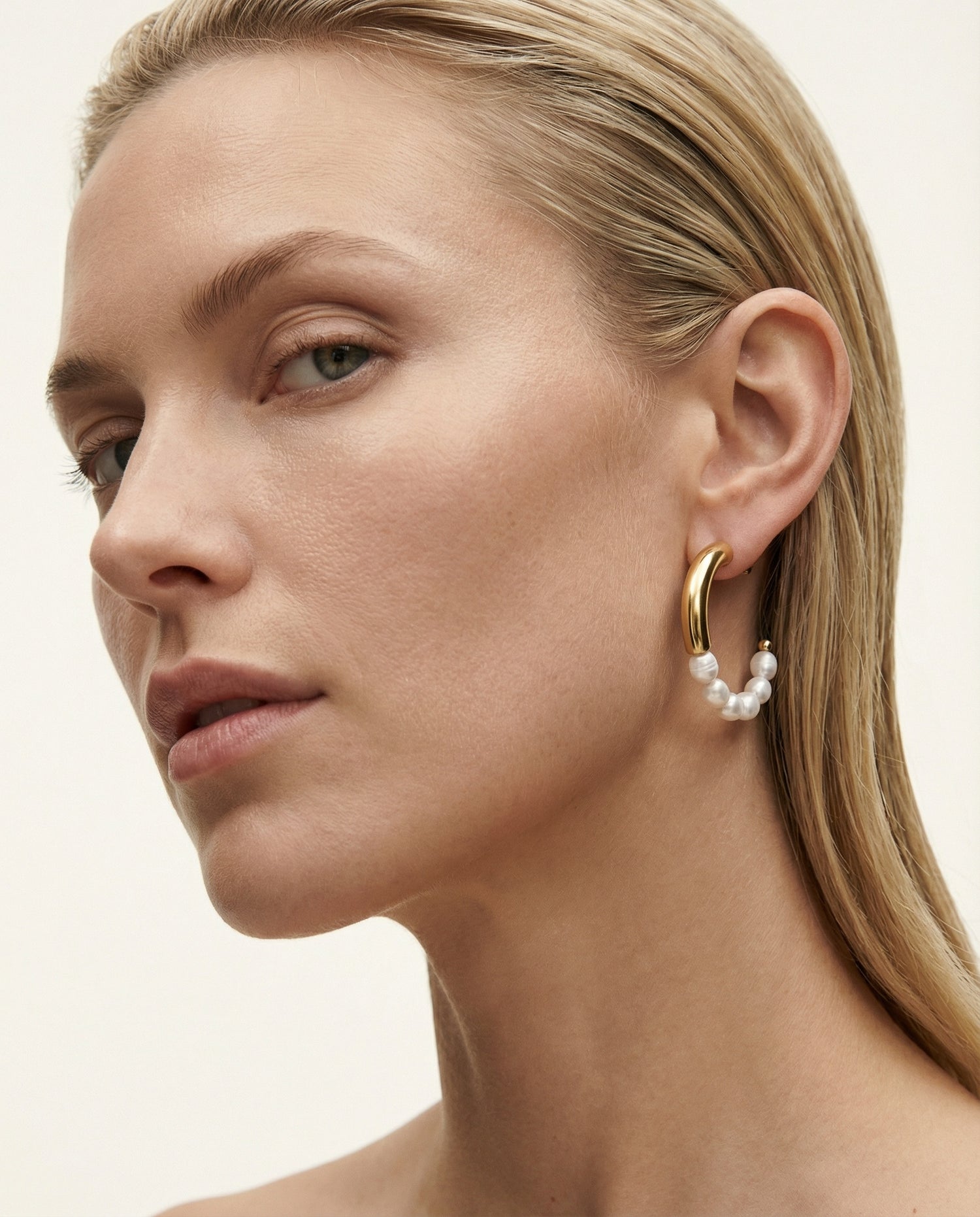 Close-up of a woman wearing gold hoop earrings with pearl accents on a neutral background