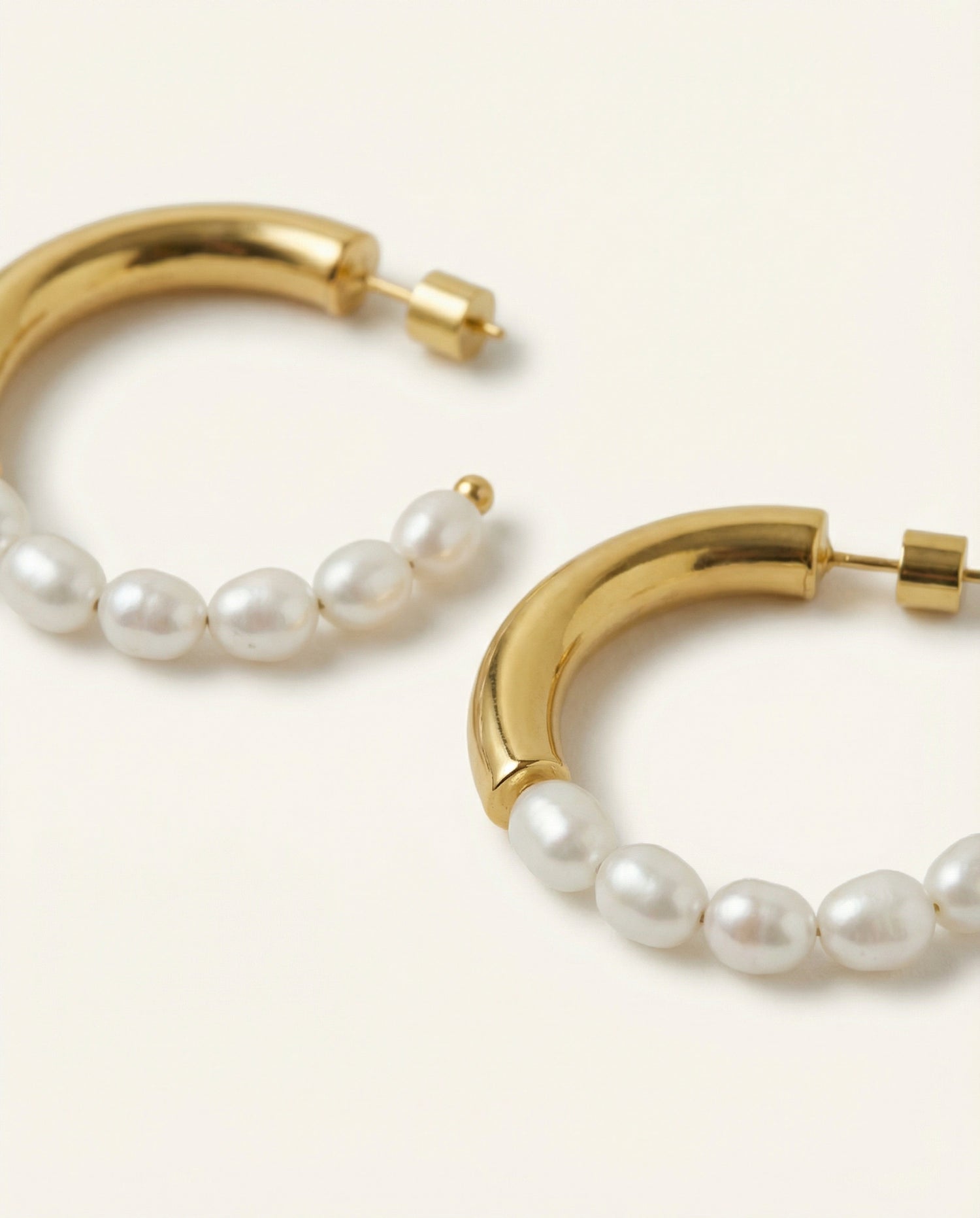 Gold hoop earrings with pearl beads on a light beige background