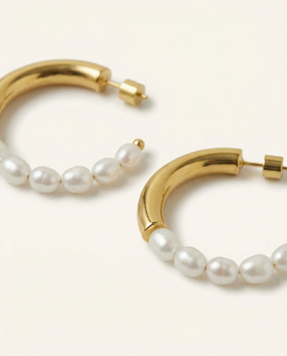 Gold hoop earrings with pearl beads on a light beige background