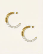 Gold hoop earrings with pearl accents on a light beige background