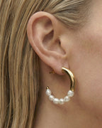 Side profile of a woman wearing a pearl earring against a plain background