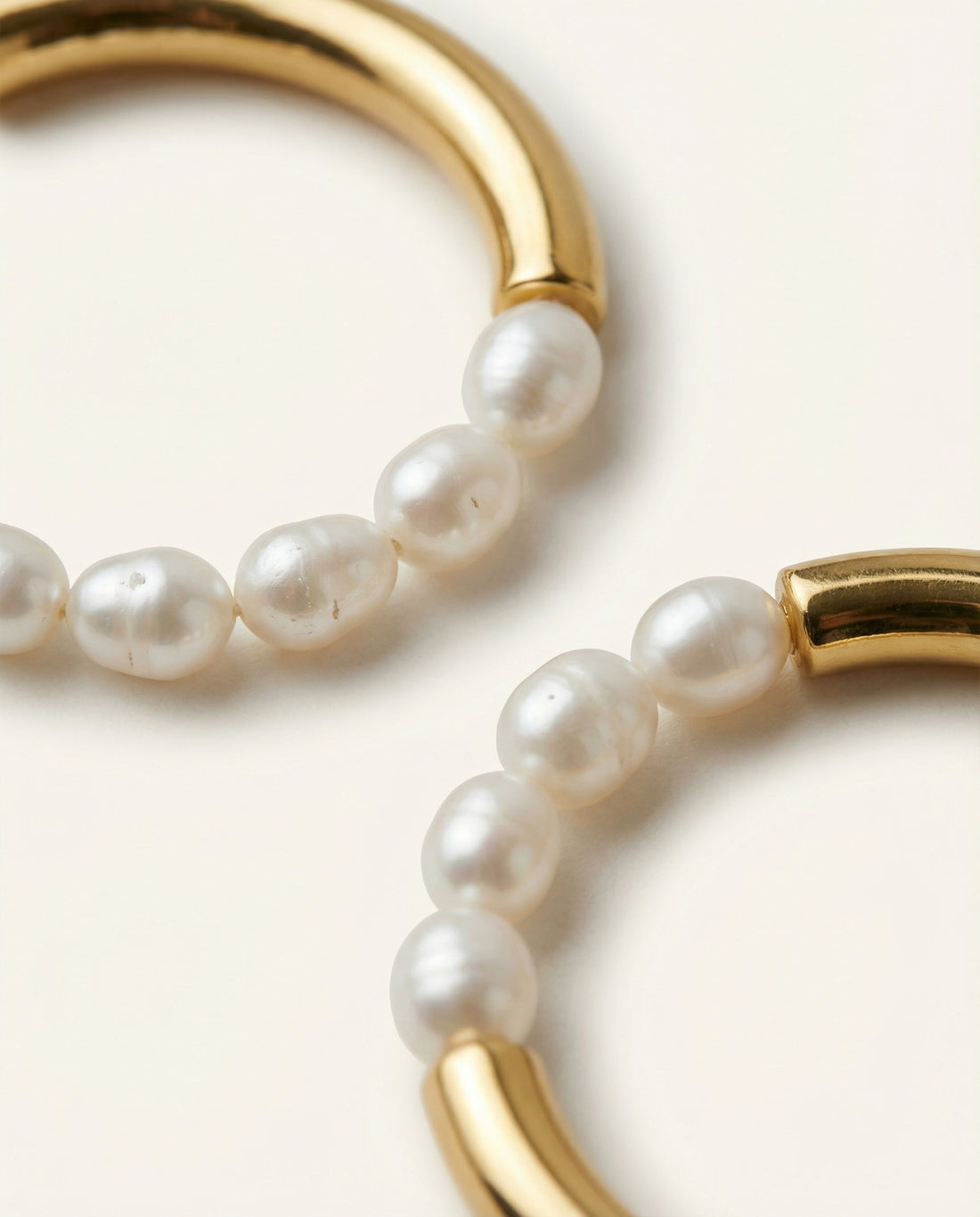 Two gold hoop earrings with pearl beads on a white background
