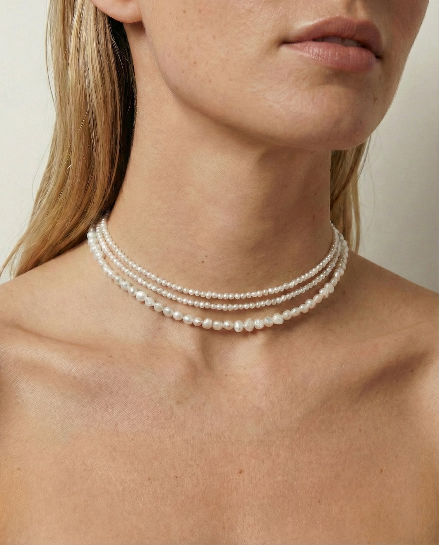 Close-up of a person wearing a pearl necklace against a neutral background
