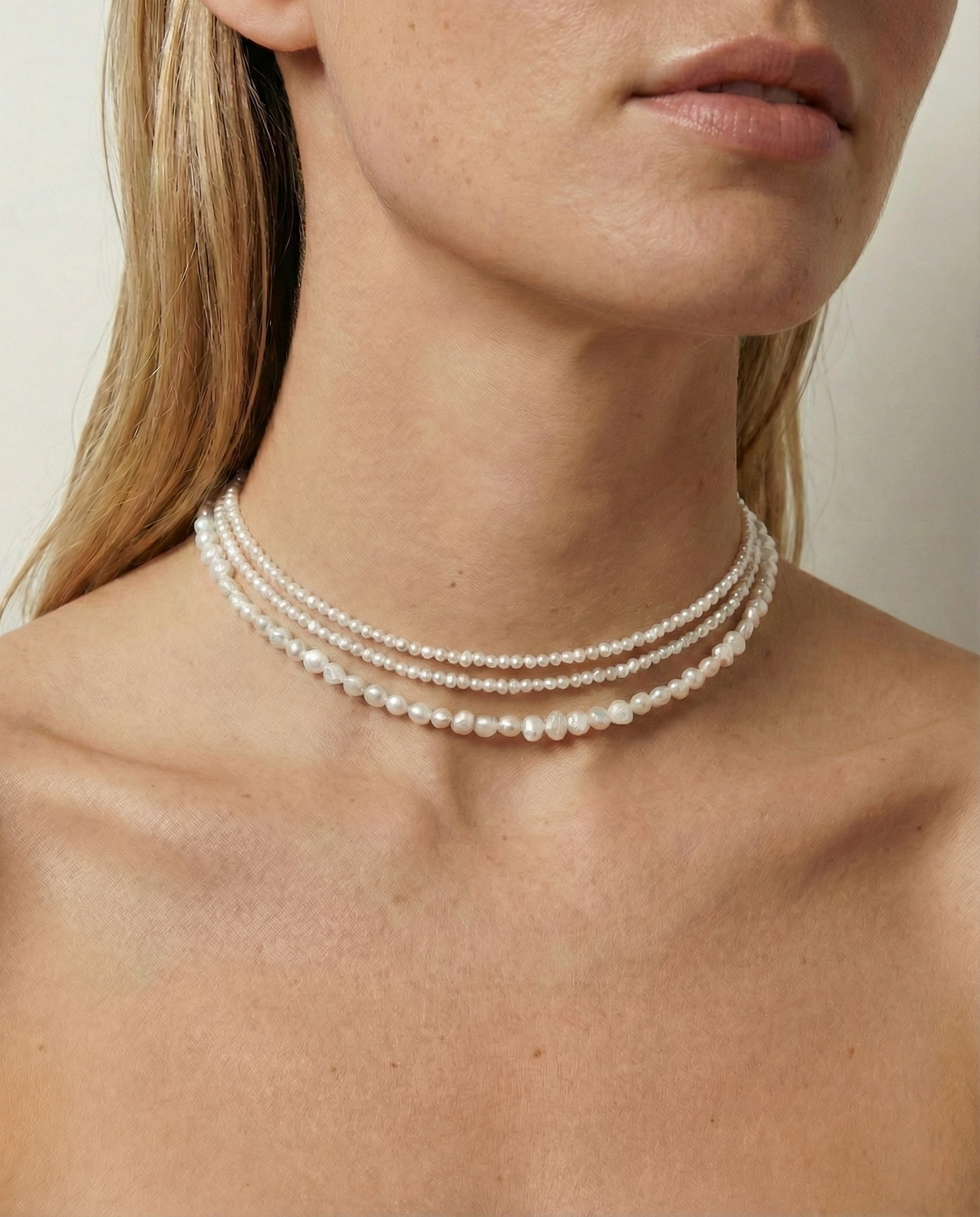 Close-up of a person wearing a pearl necklace against a neutral background