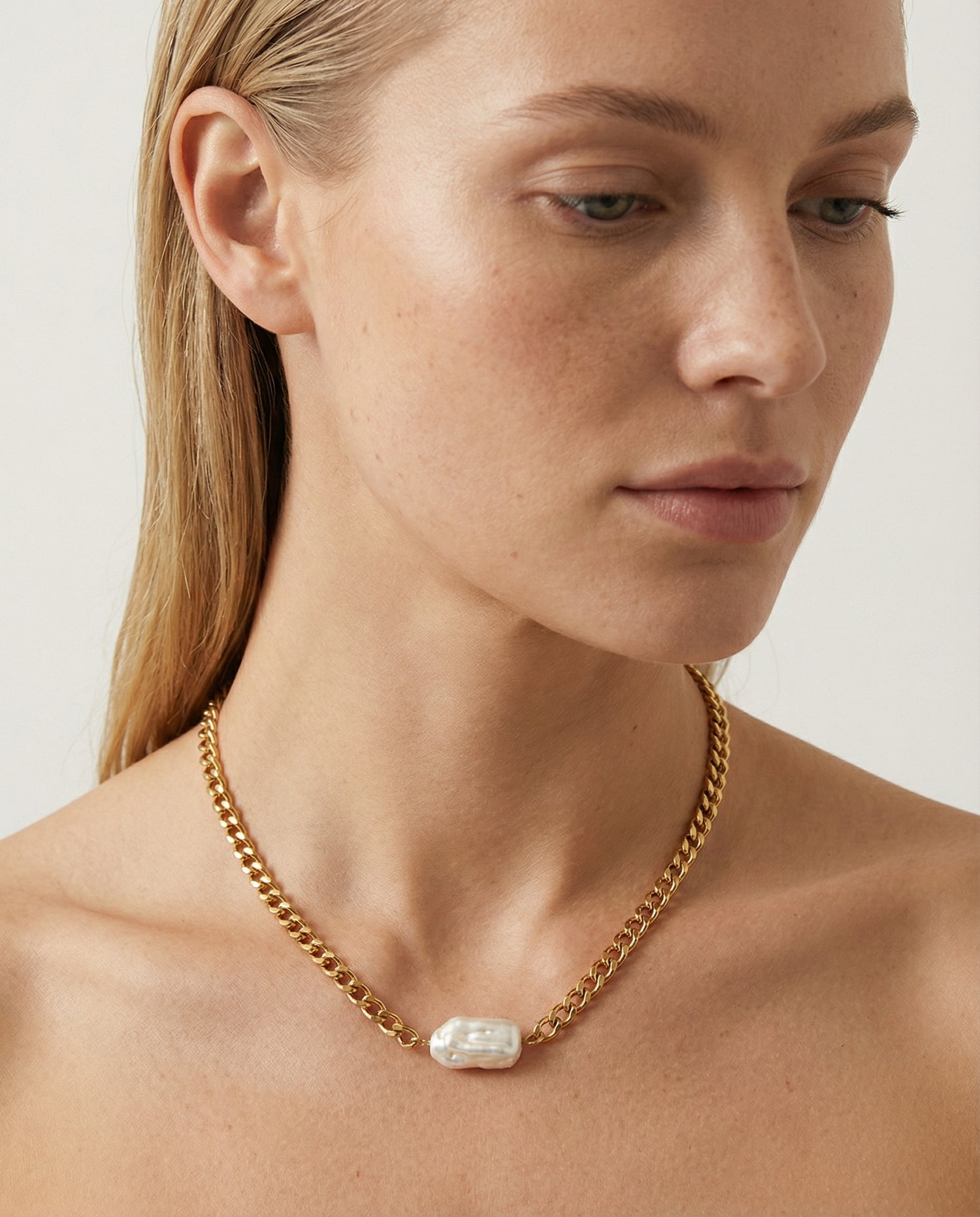 Woman wearing a gold chain necklace with a clear pendant on a neutral background