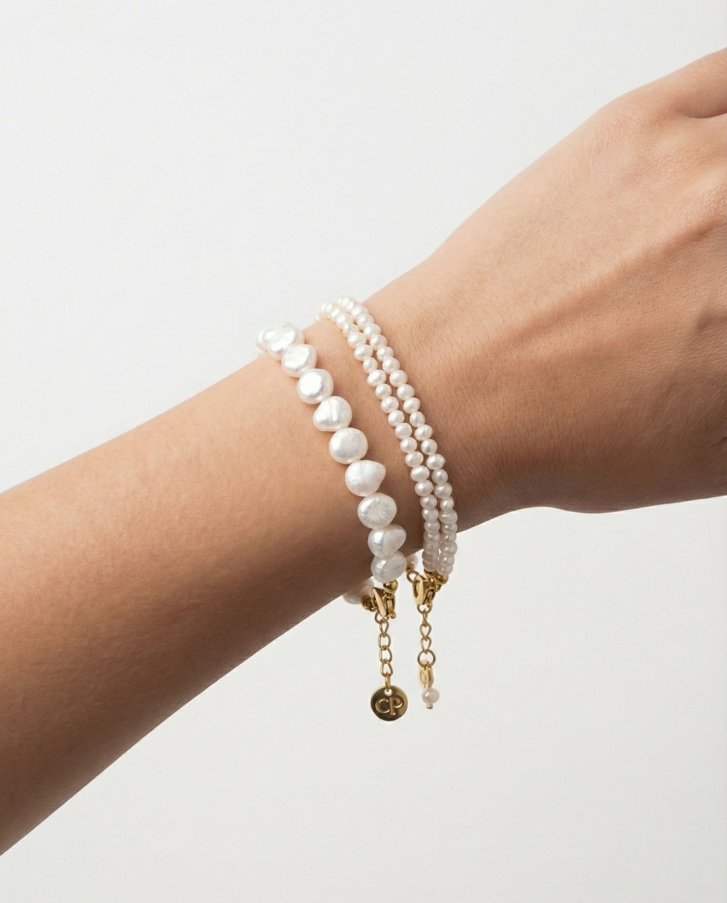 Two pearl bracelets on a wrist against a light gray background