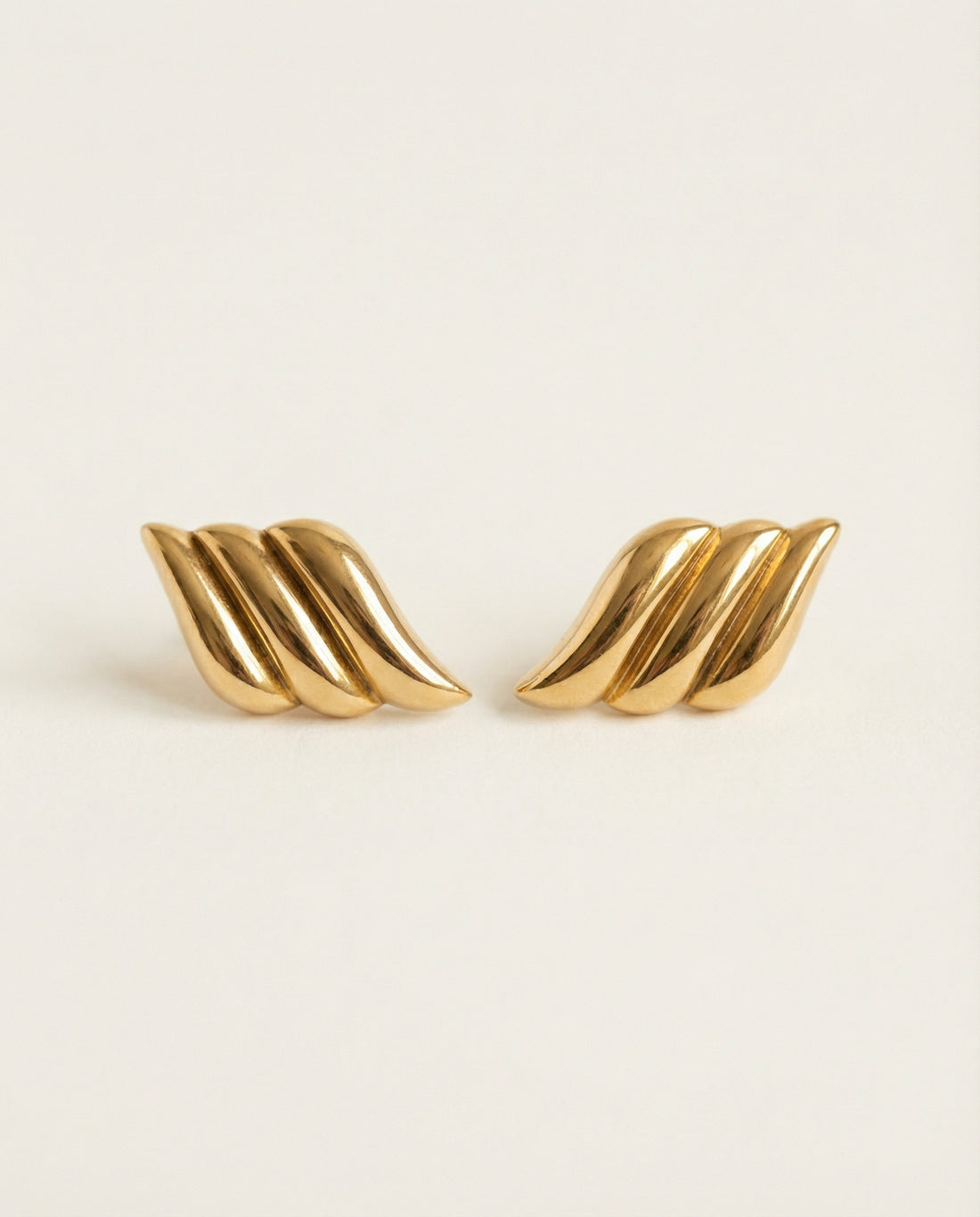 Pair of gold wing-shaped earrings on a beige background