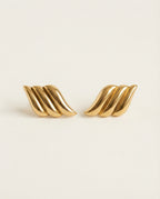 Pair of gold wing-shaped earrings on a beige background